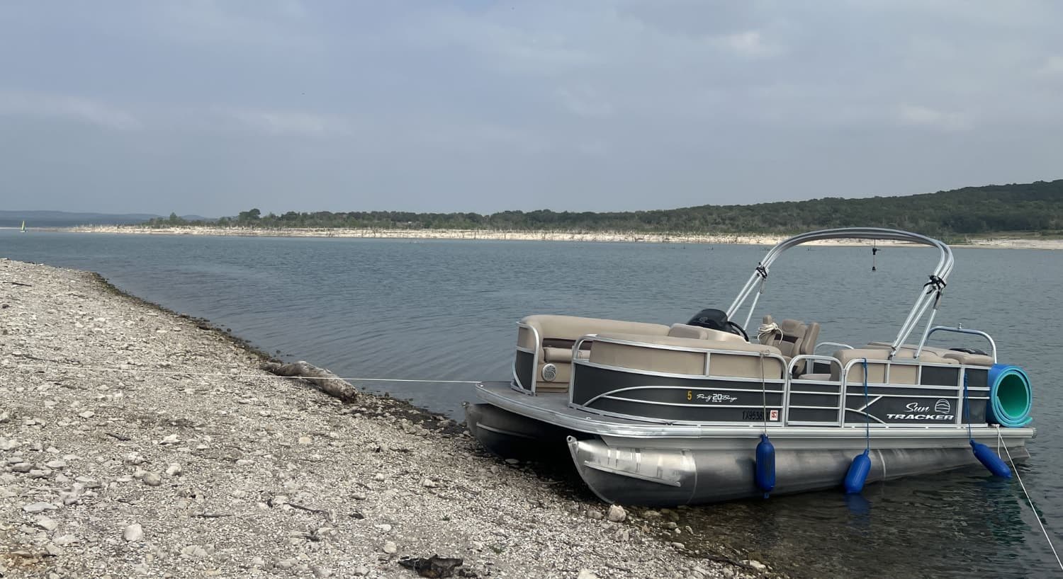 Gray and tan pontoon boat docked on the shore