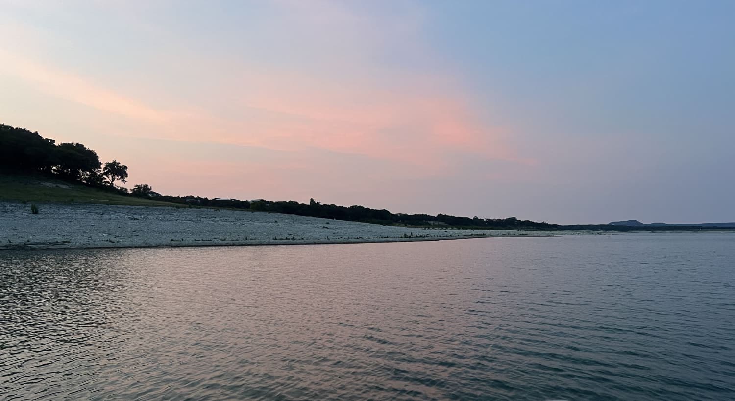 Body of water with the shoreline and trees in the background at dusk