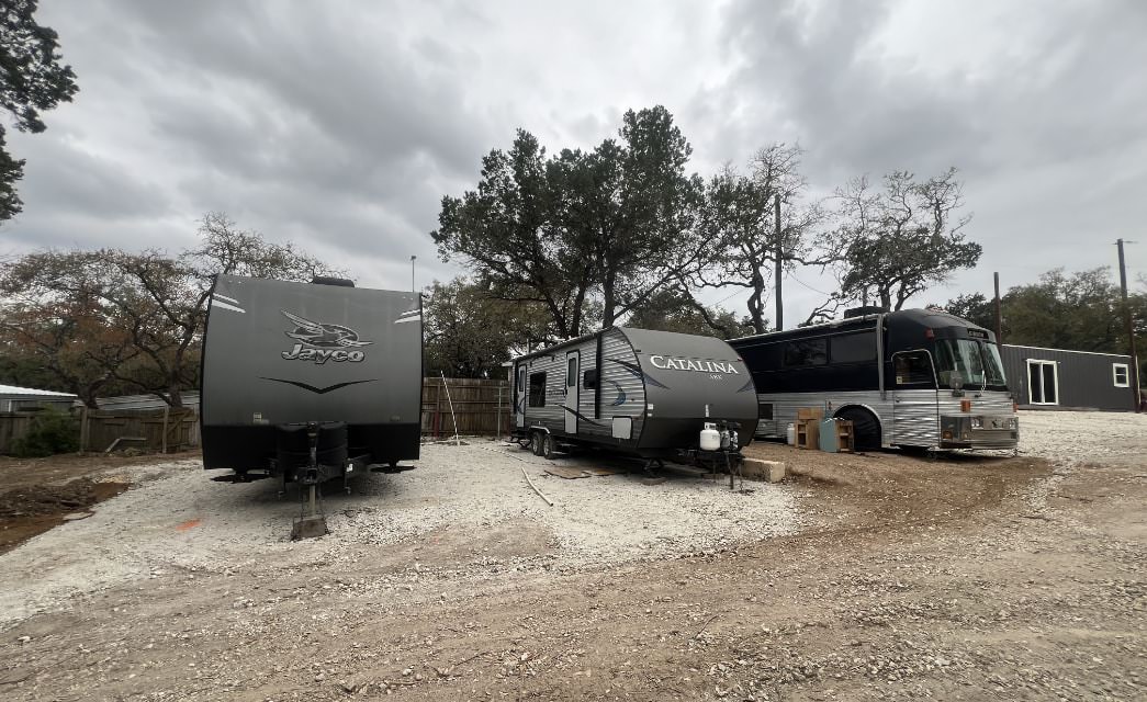 Two long campers and a bus parked side by side on gravel