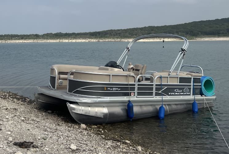 Gray and tan pontoon boat docked on the shore