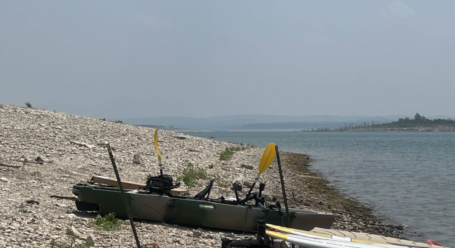 Green and tan fishing kayak on the shore next to a body of water